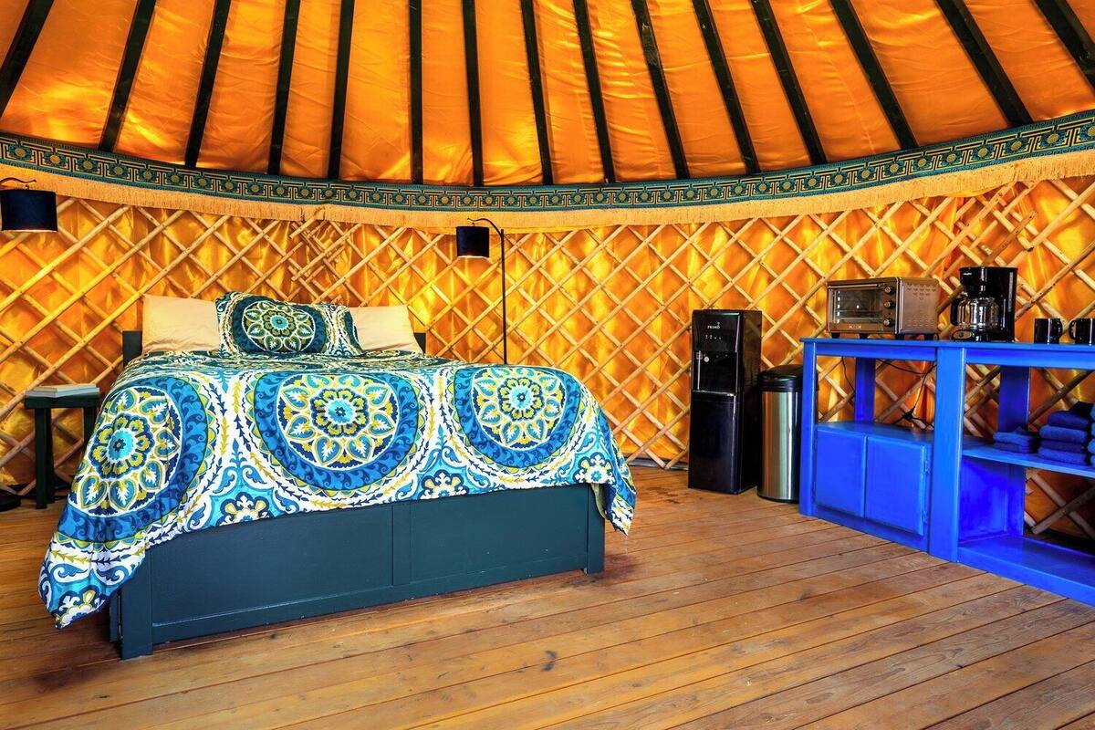A yurt with a bed, a small table, and a blue cabinet.