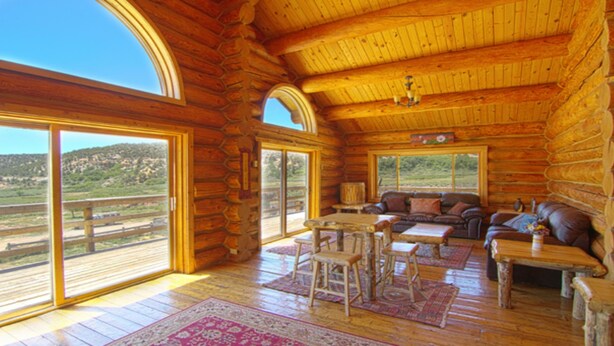 A log cabin with large windows, a wooden ceiling, a sofa, a table, and a chair. - Boulder Mountain Guest Ranch (Boulder)