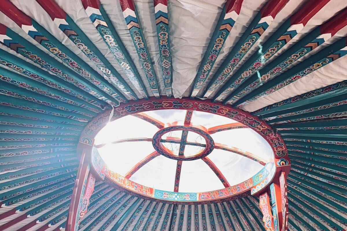A room with a bed under a decorative canopy, a green sofa, and a colorful artwork on the floor.