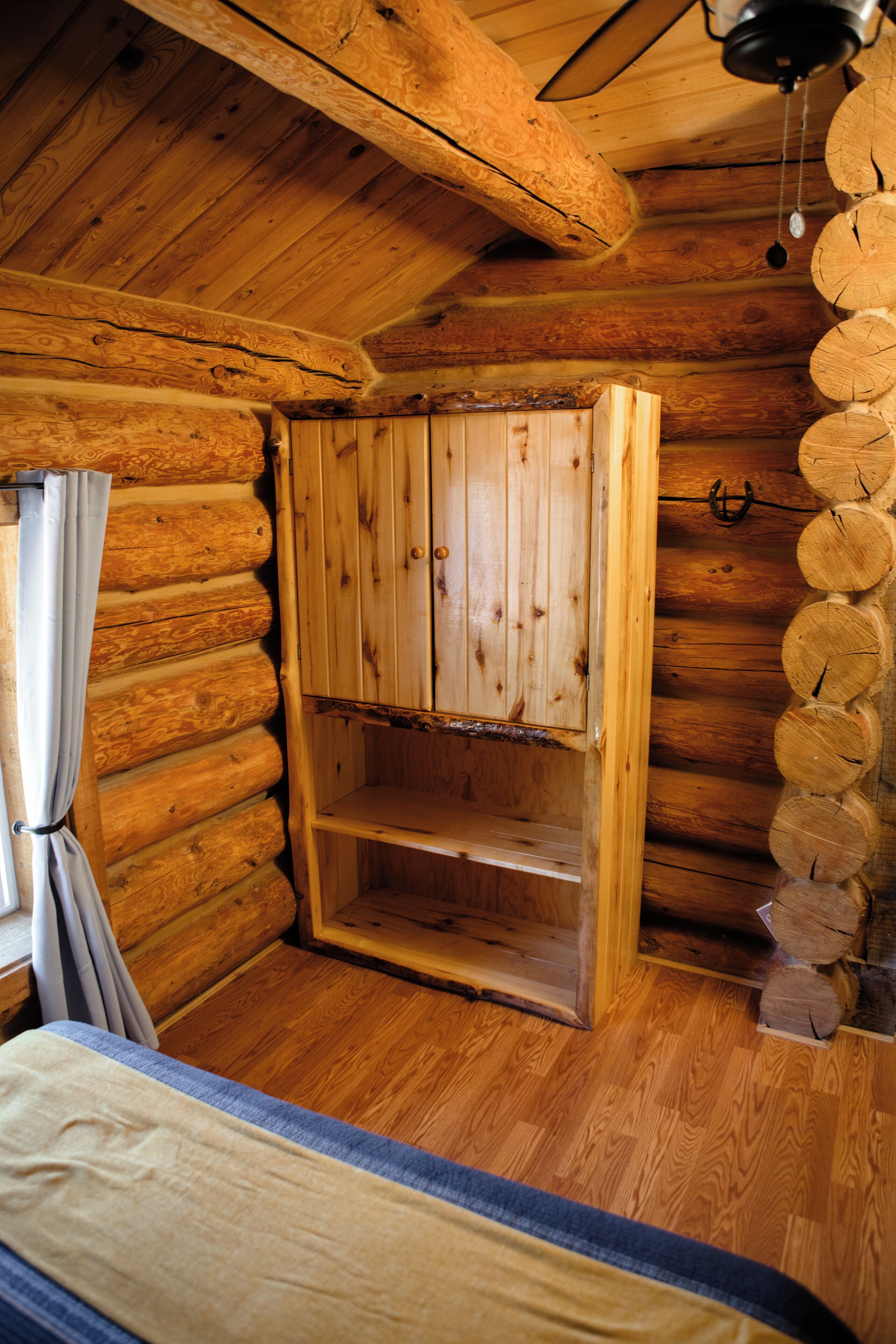 A log cabin room with a wooden bed, a wooden wardrobe, and a ceiling fan.