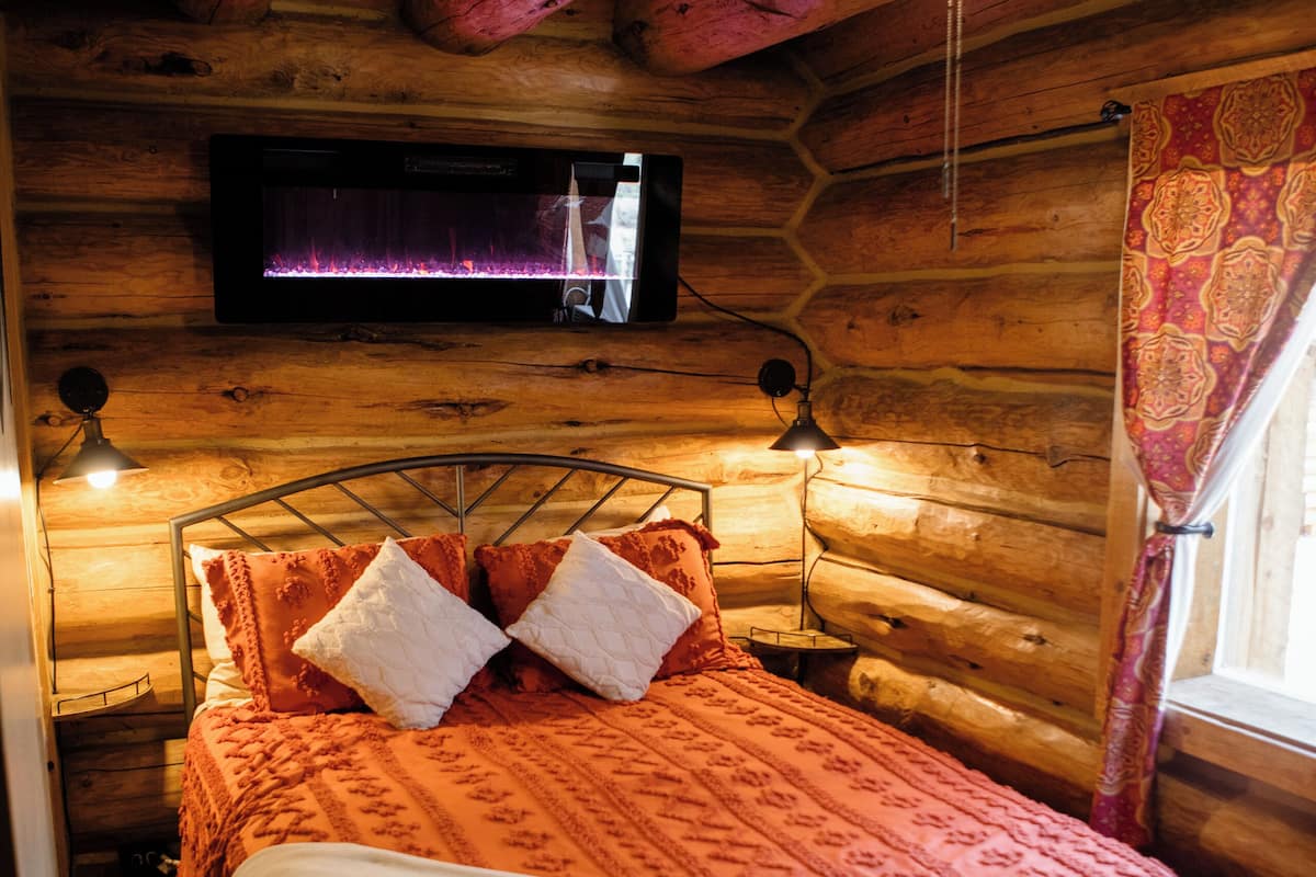 A wooden cabin room with a bed, a ceiling fan, a mounted TV, and two bedside lamps.