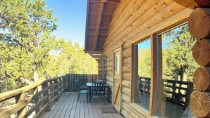 A wooden deck with a grill, wooden logs, and a view of trees. - Boulder Mountain Guest Ranch (Boulder)