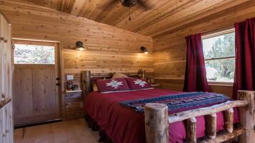 Een gezellige slaapkamer in een blokhut, met een houten bed, een raam met rode gordijnen en een deur met een klein raampje.