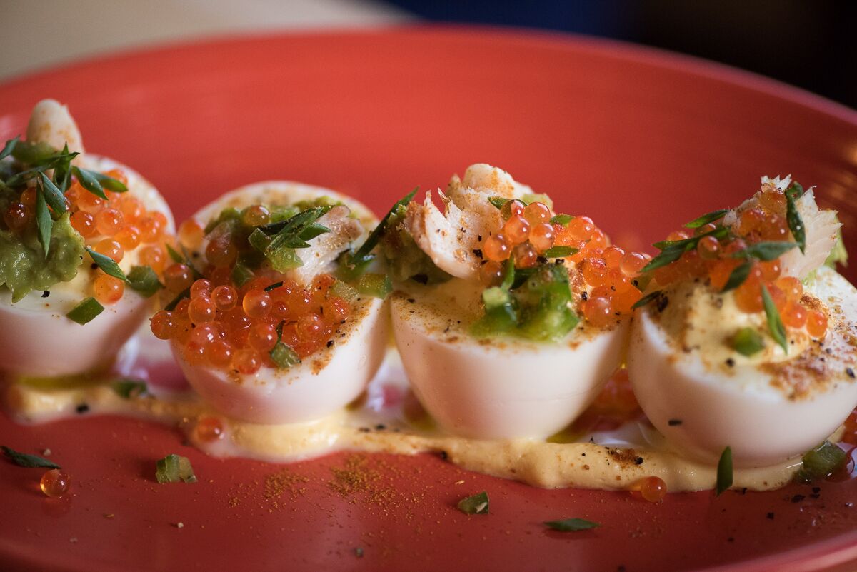 A dish with poached eggs, caviar, and herbs on a red plate.