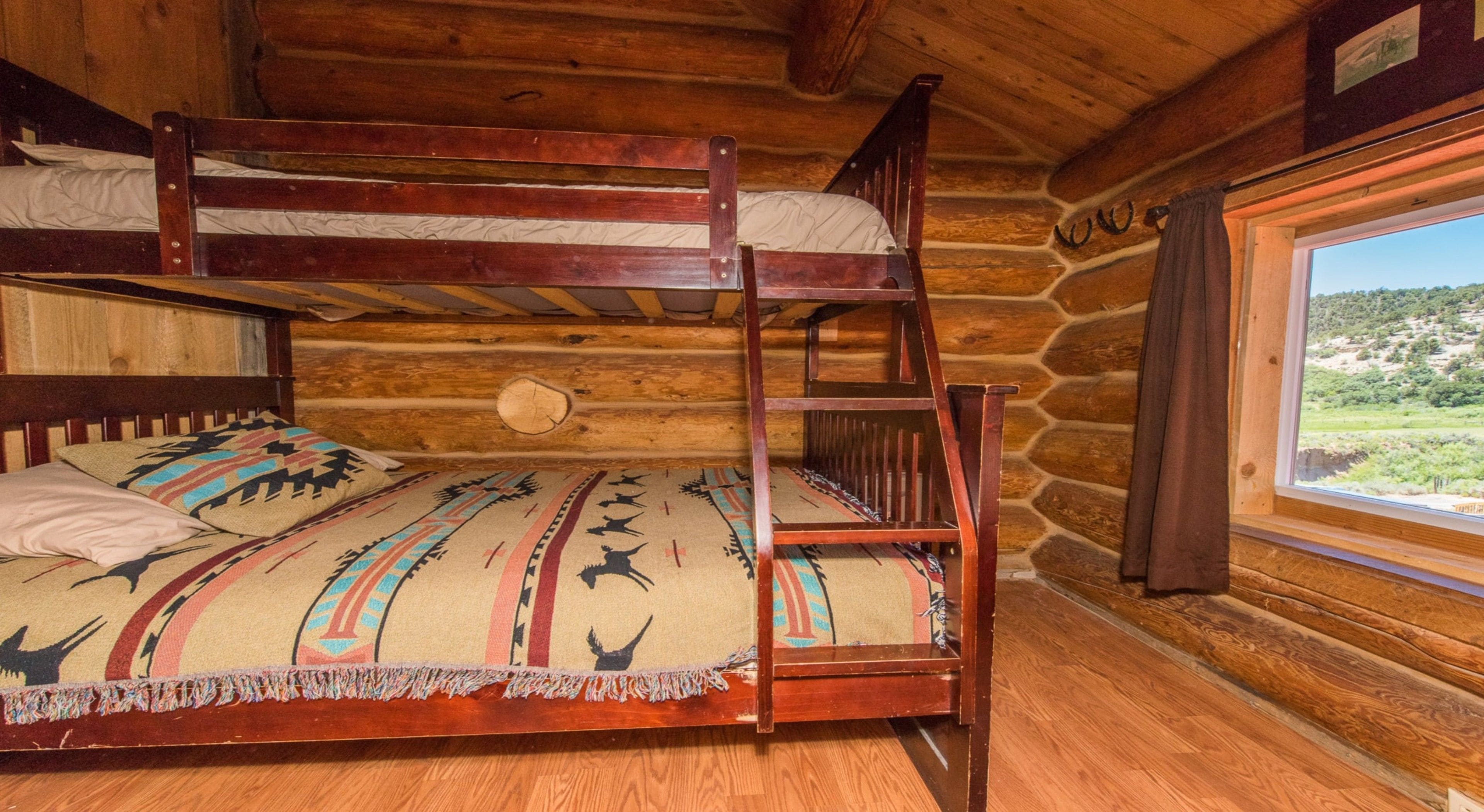 Ein Stockbett mit einem gemusterten Bettbezug und Kissen, Holzwände, einem Fenster mit Landschaftsblick und einem Holzboden.