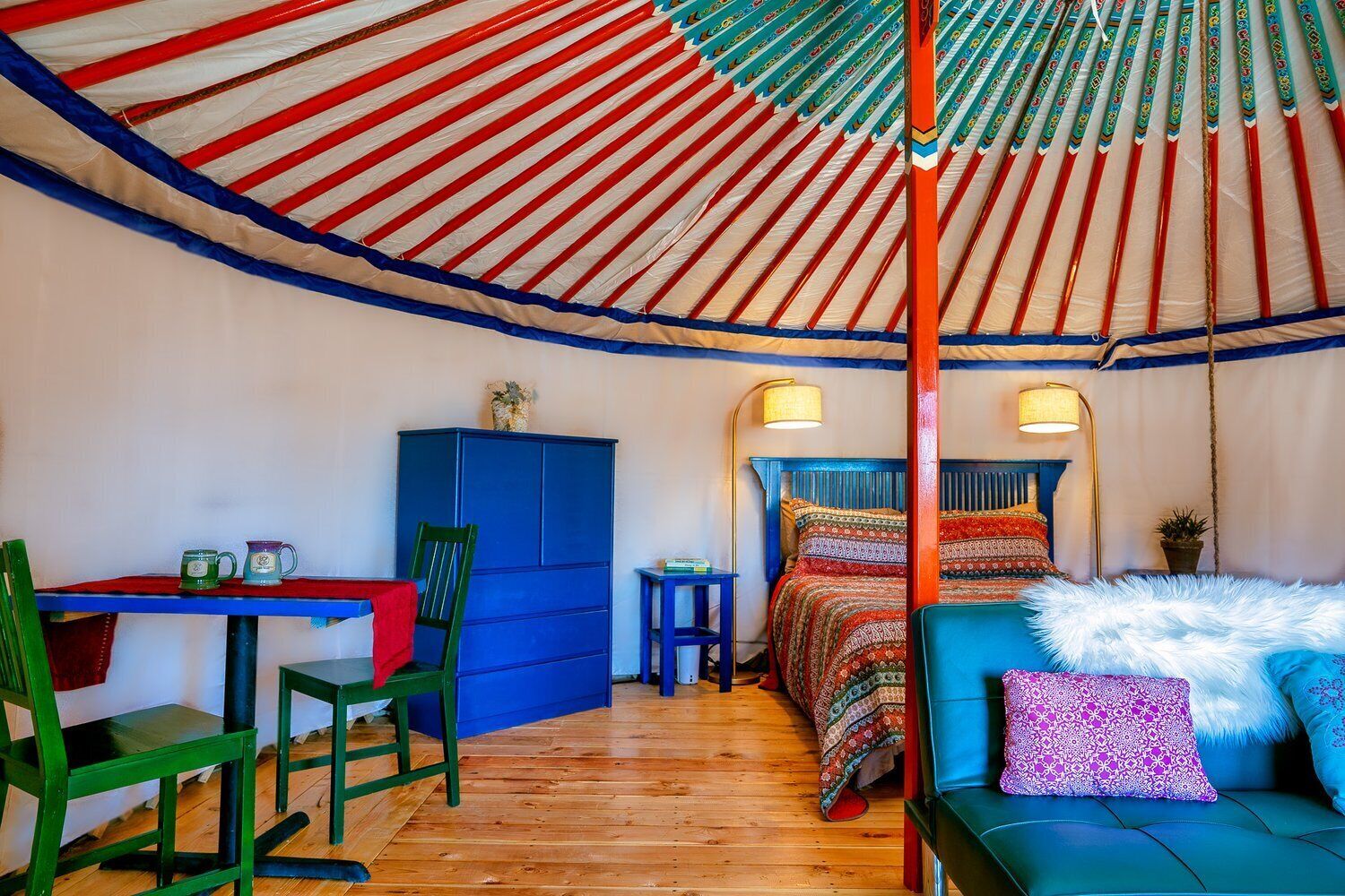 A cozy room with a wooden floor, a bed with patterned bedding, a blue cabinet, and a table with two mugs.