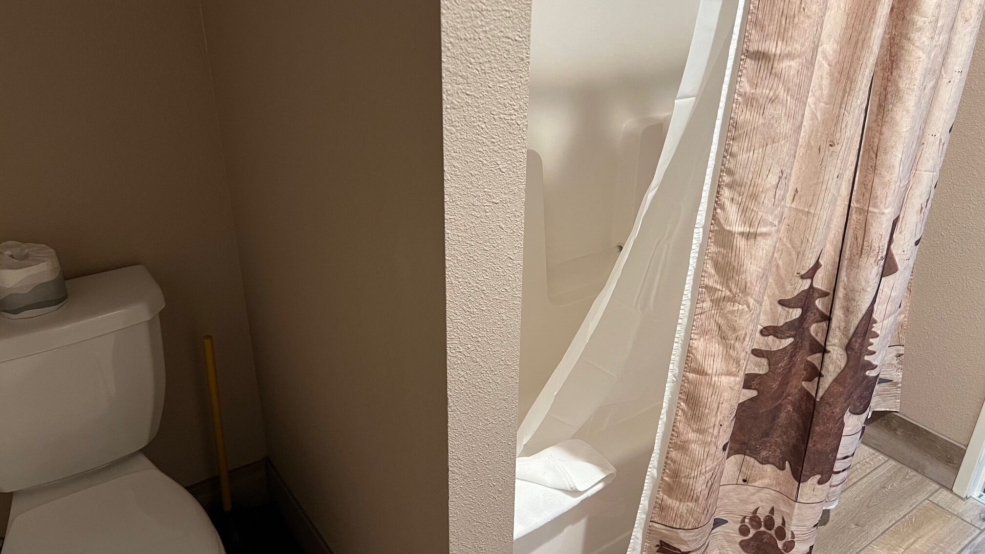 Un baño con inodoro, escoba y cortina de ducha estampada con hojas.