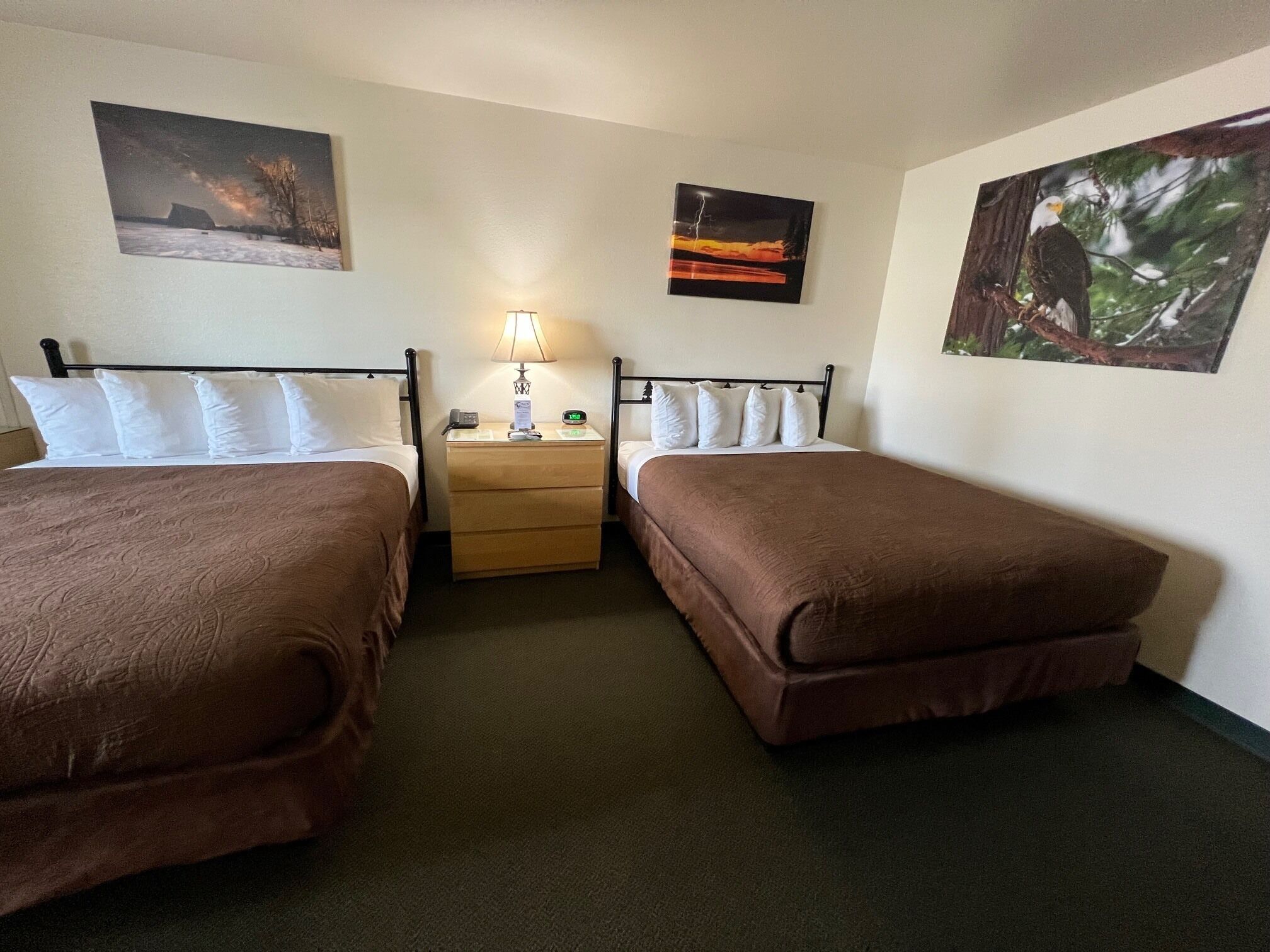 Une chambre d’hôtel avec deux lits simples, une table de chevet avec une lampe et trois tableaux accrochés au mur.