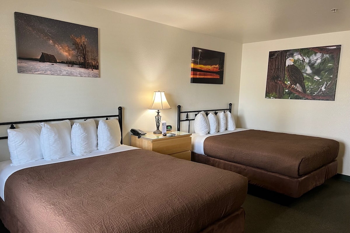 A hotel room with two beds, a nightstand with a lamp, and three wall-mounted pictures.