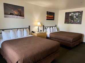 Habitación de hotel con dos camas, una mesita de noche con lámpara y tres cuadros colgados en la pared.