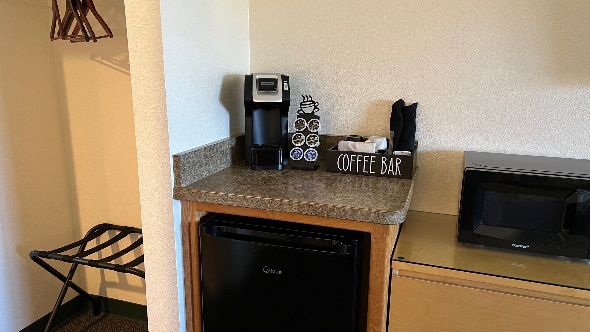 A kitchenette with a coffee maker, a coffee bar sign, and a microwave.
