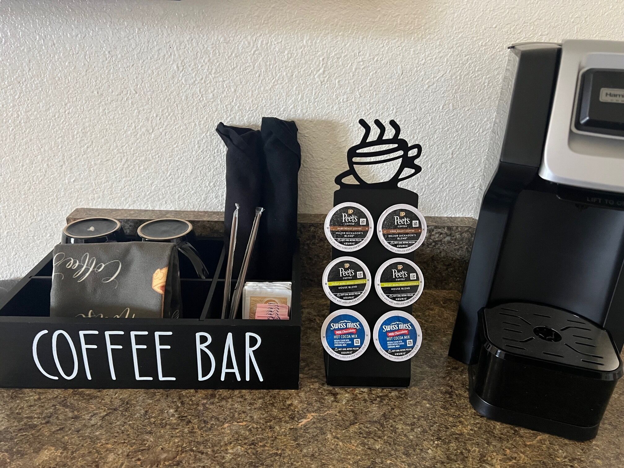 Un espace café aménagé avec une machine à café, une cafetière et un présentoir de dosettes de café.