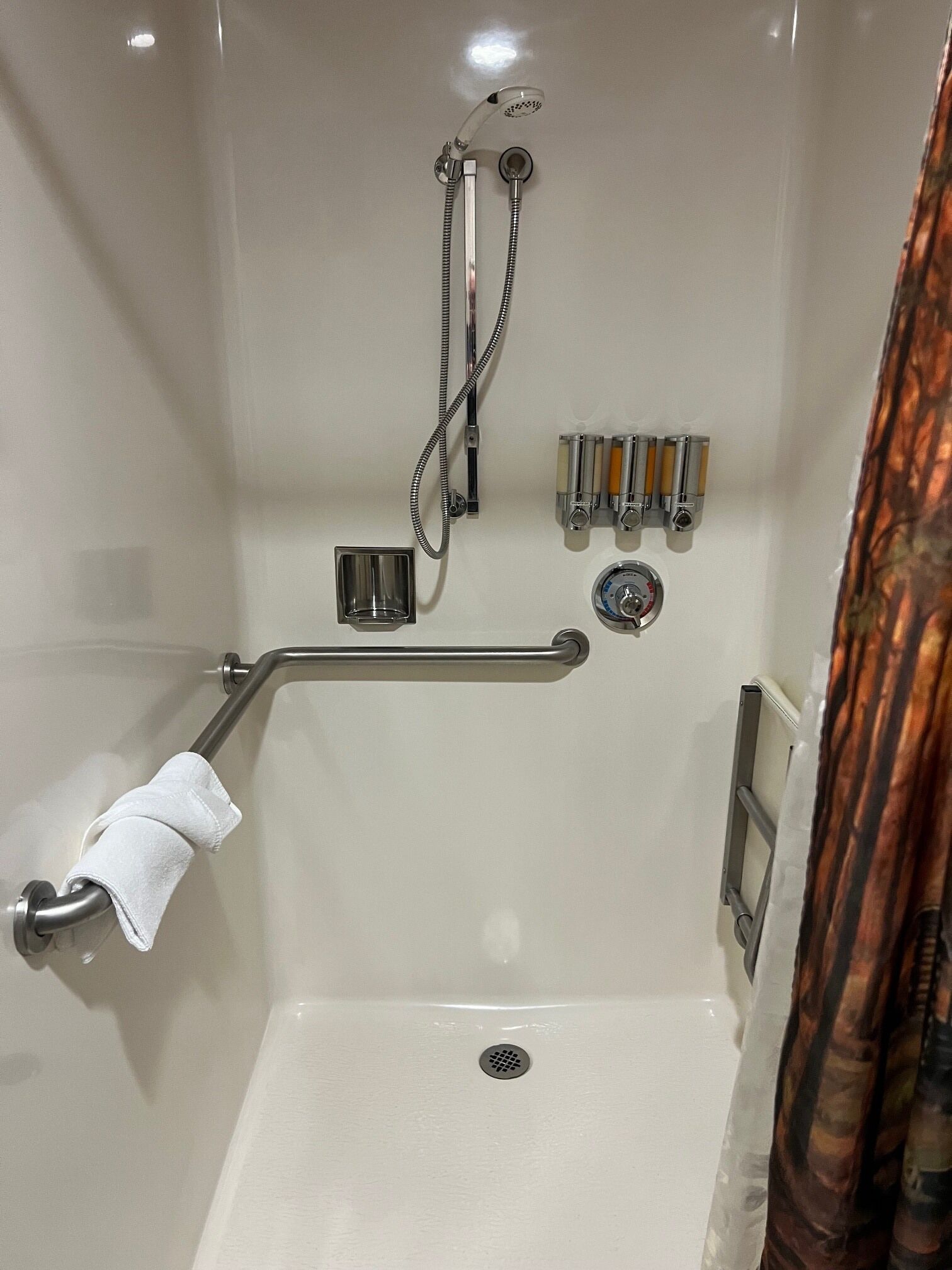 A shower with a handheld showerhead, a handheld shower attachment, a grab bar, and a towel rack.