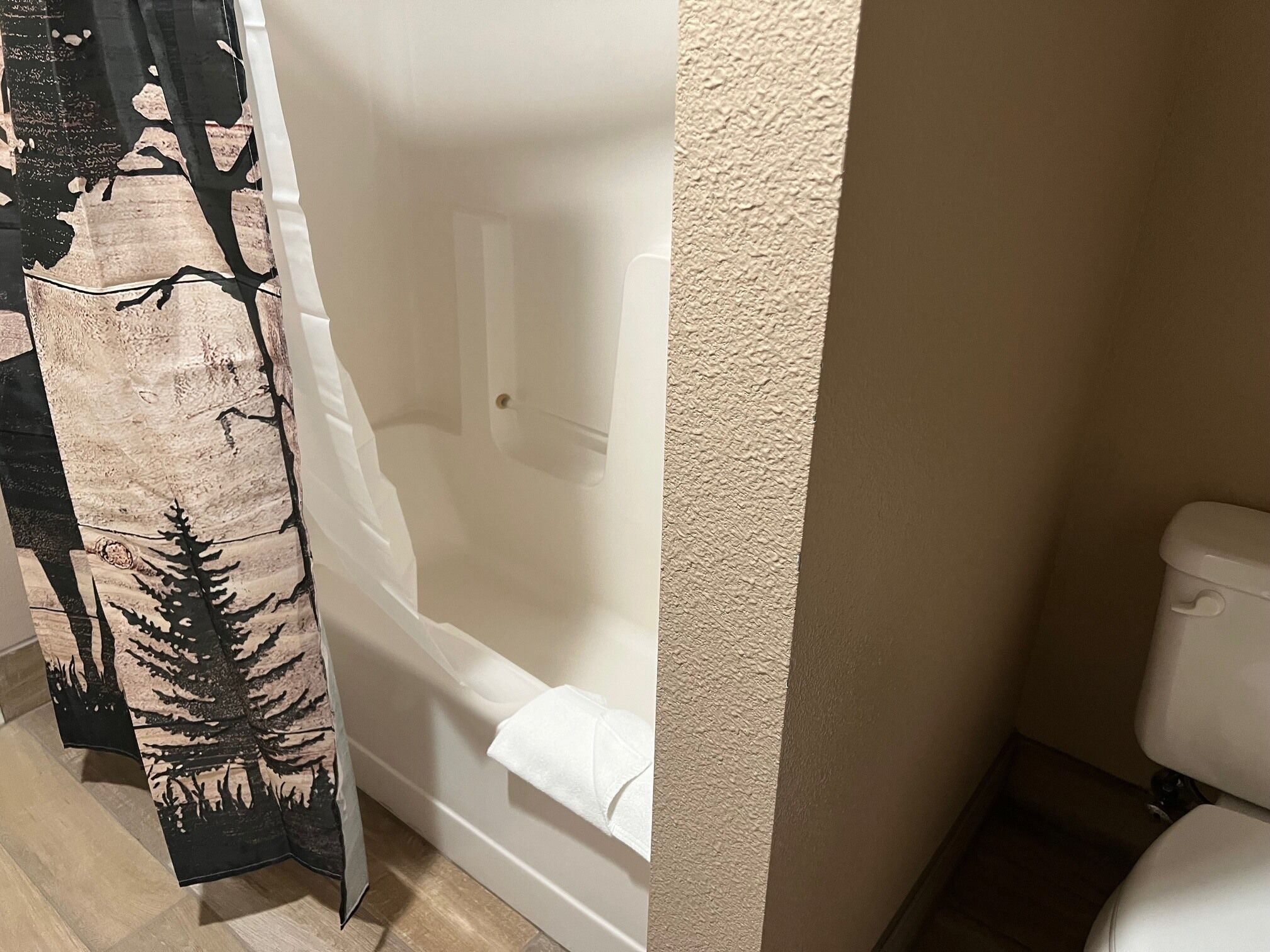 A bathroom with a bathtub, toilet, and a shower curtain with a forest design.