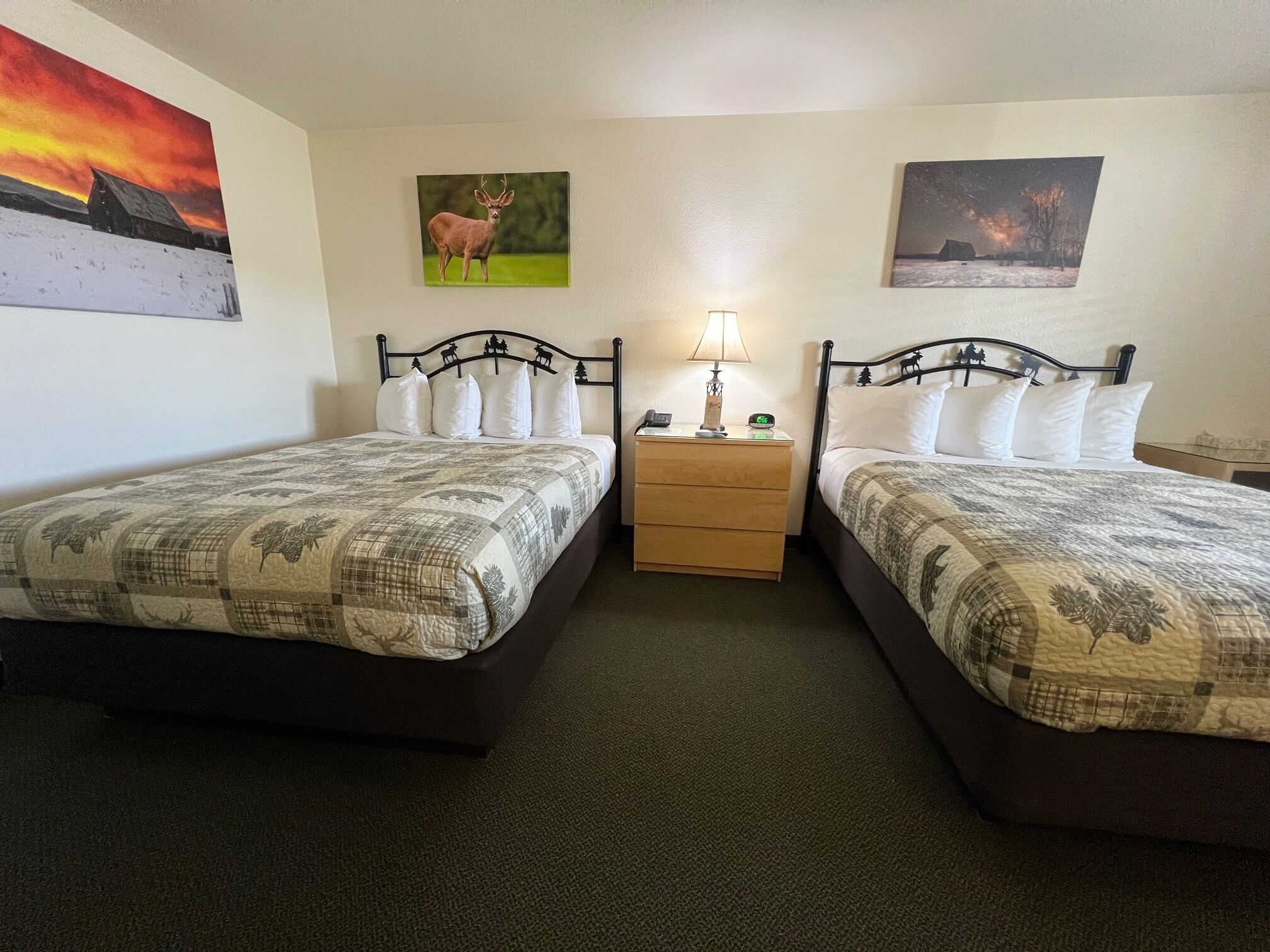A hotel room with two beds, a nightstand with a lamp, and two wall-mounted paintings.