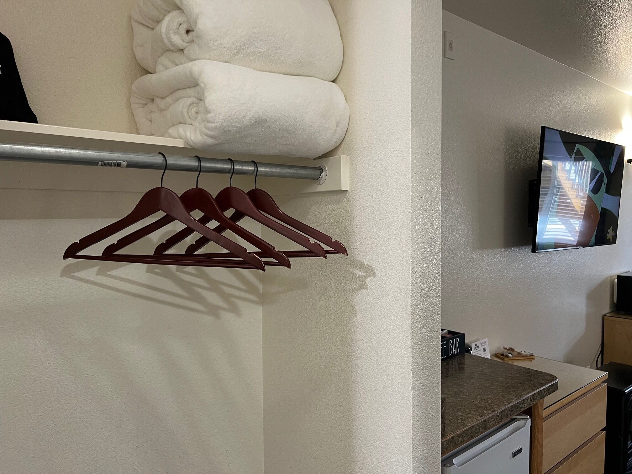 A hotel room with a neatly folded white towel stack, a wall-mounted TV, and a countertop with a coffee machine.