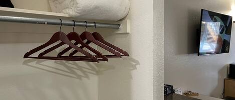 A hotel room with a neatly folded white towel stack, a wall-mounted TV, and a countertop with a coffee machine.