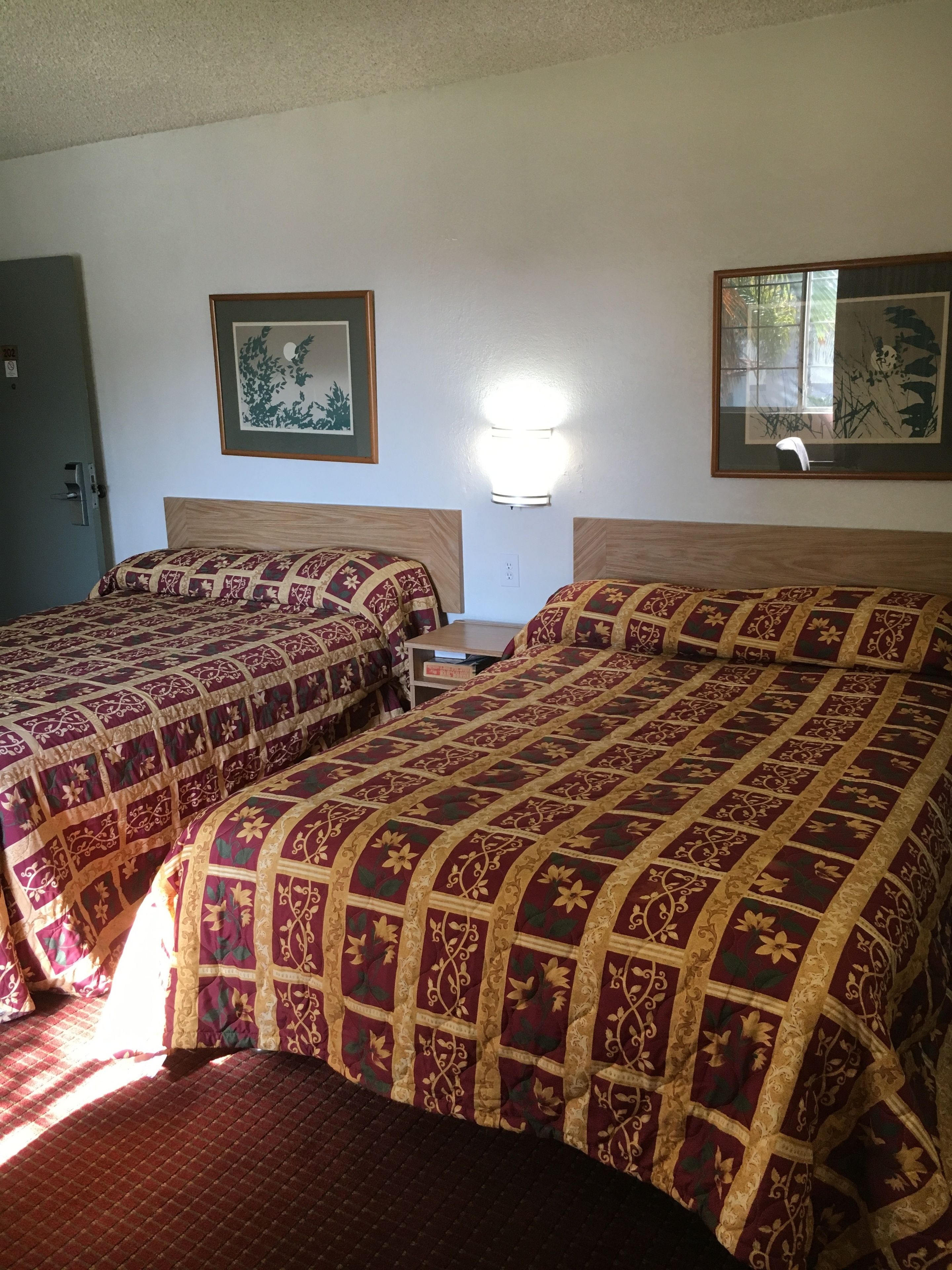 Two beds with patterned bedding, a wall-mounted light, and framed artwork.