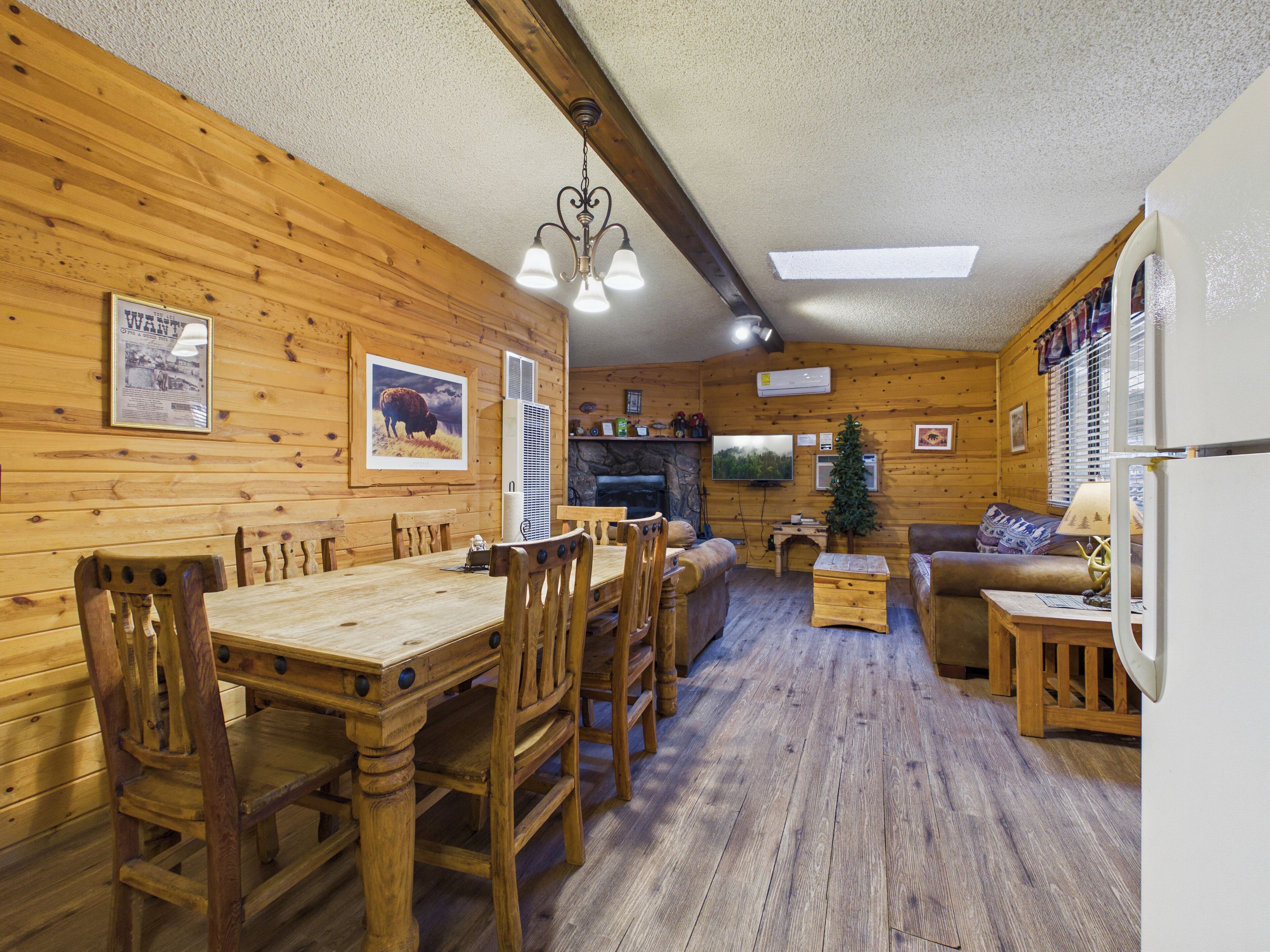 A wooden interior with a dining table, chairs, a sofa, and a television.