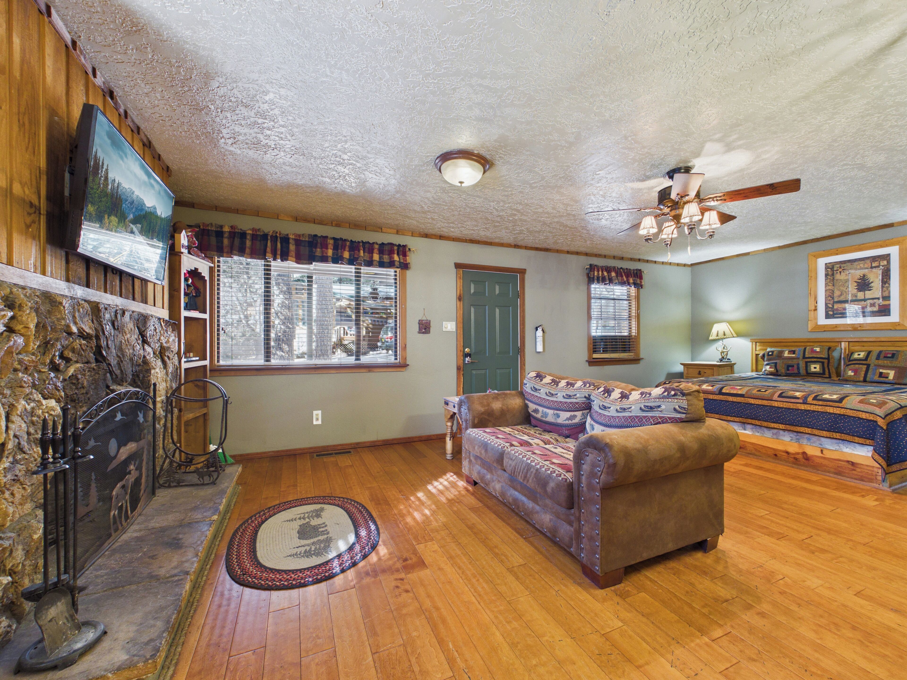 A cozy living room with a fireplace, a sofa, a television, and a ceiling fan.