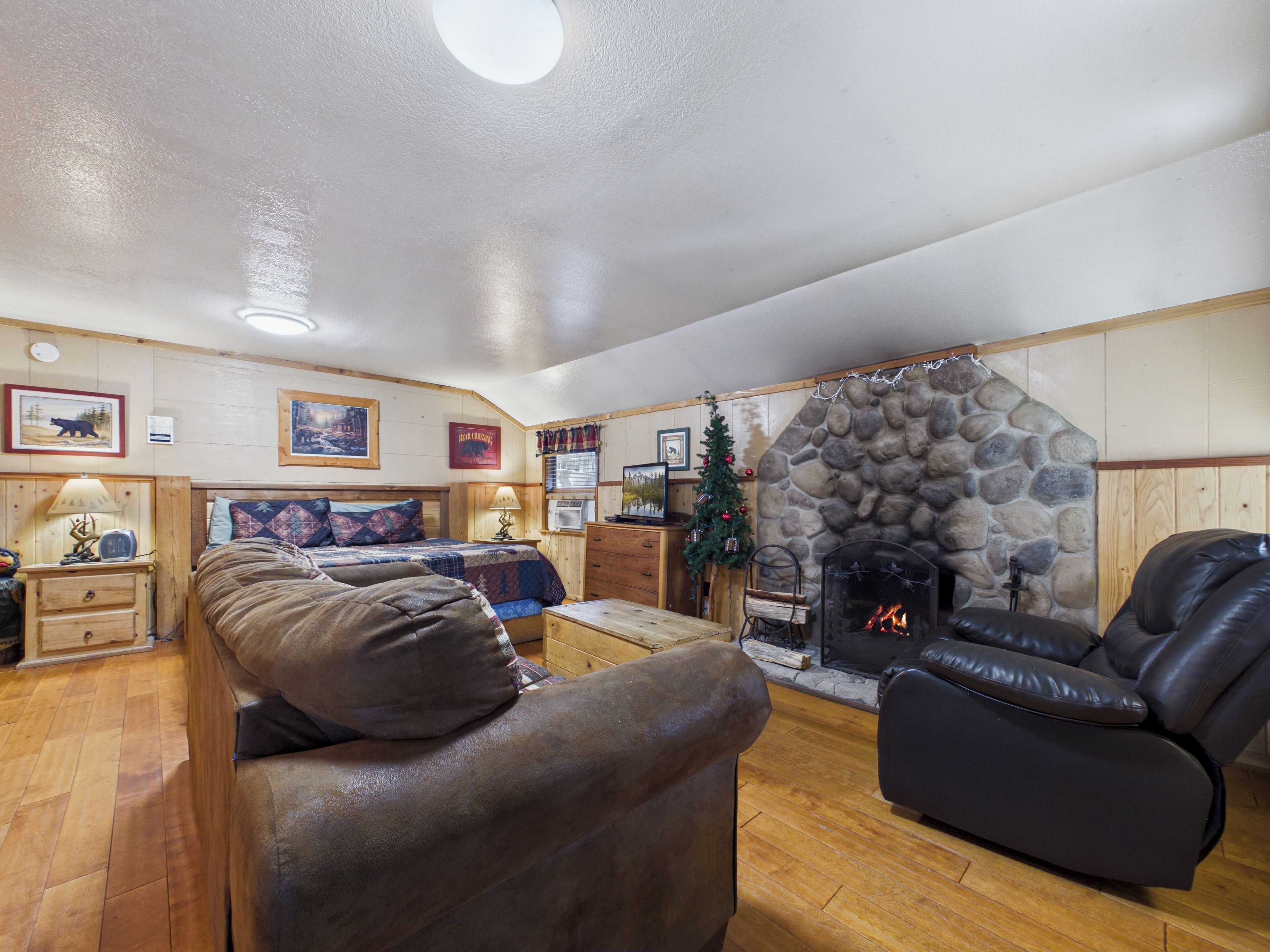 A cozy living room with a stone fireplace, leather sofas, wooden floors, and a Christmas tree.
