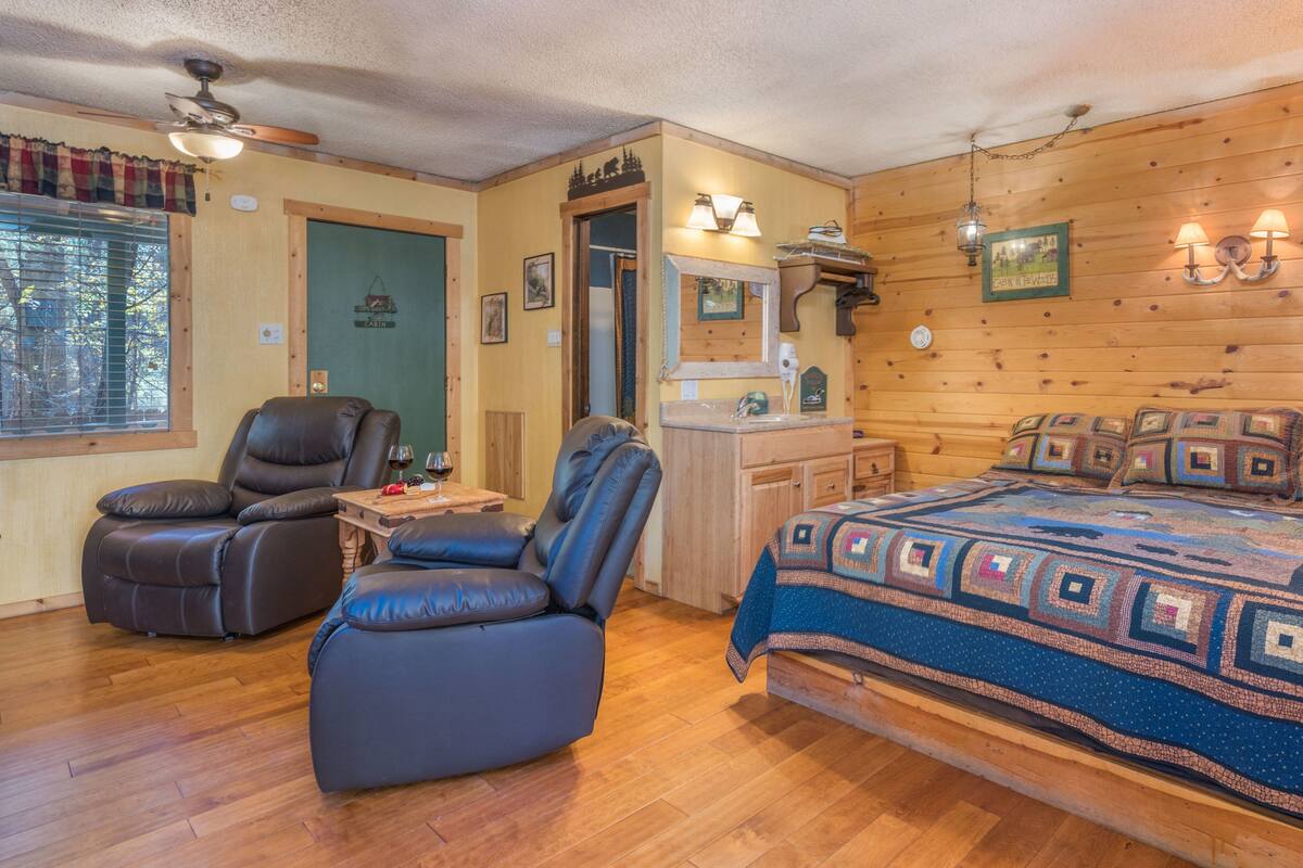 Une chambre confortable dans un chalet, avec un lit, deux fauteuils inclinables en cuir, une commode en bois et une fenêtre avec des stores.