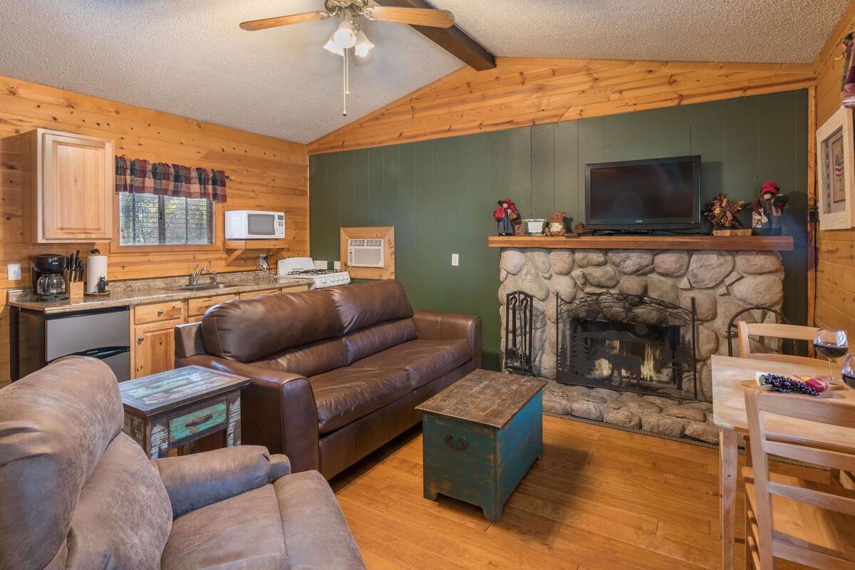 L’intérieur chaleureux d’un chalet avec une cheminée en pierre, un canapé en cuir, une table à manger en bois et un téléviseur placé au-dessus de la cheminée.