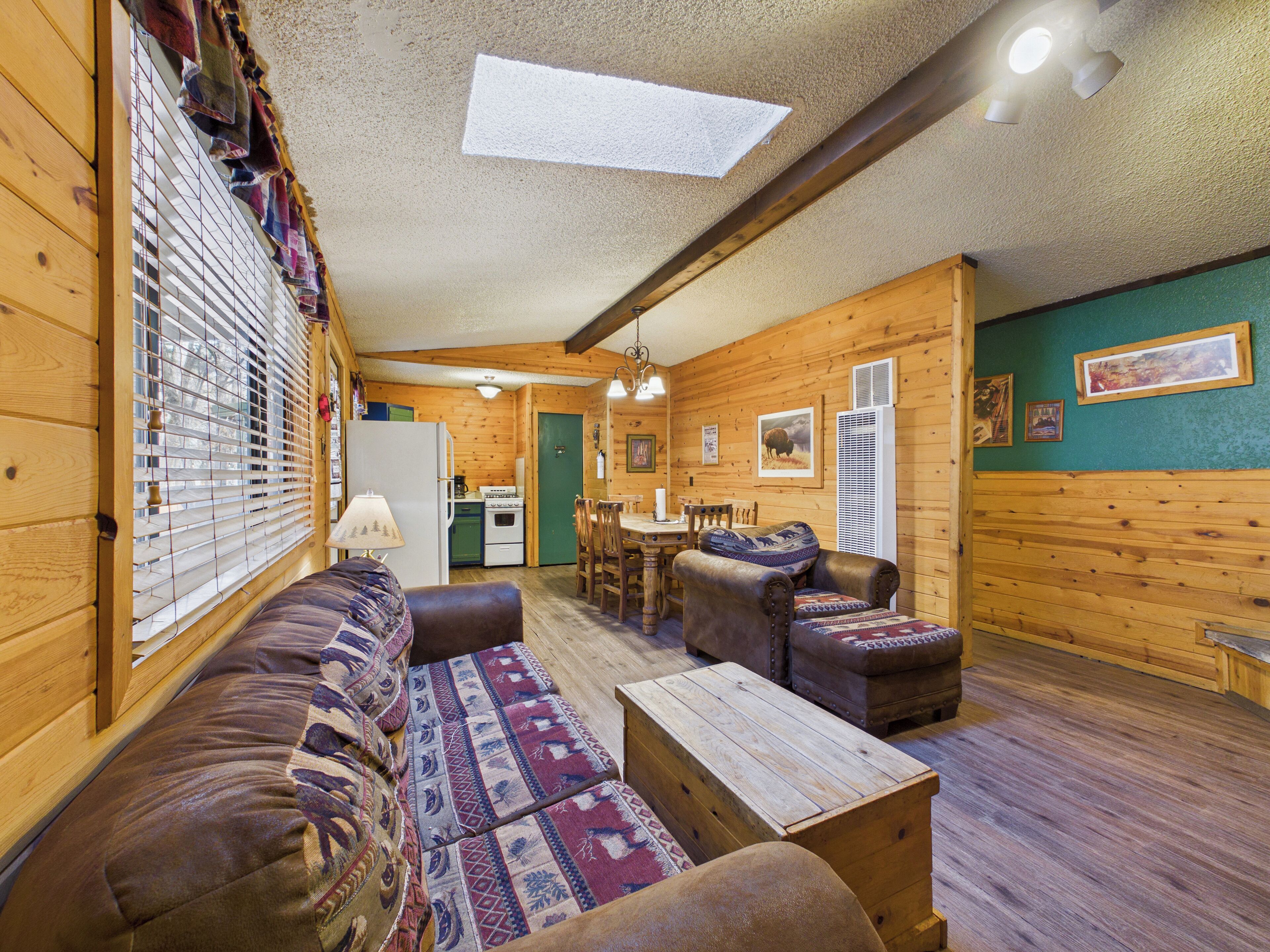 A cozy cabin interior with a sofa, a wooden coffee table, a dining area, and a kitchen.