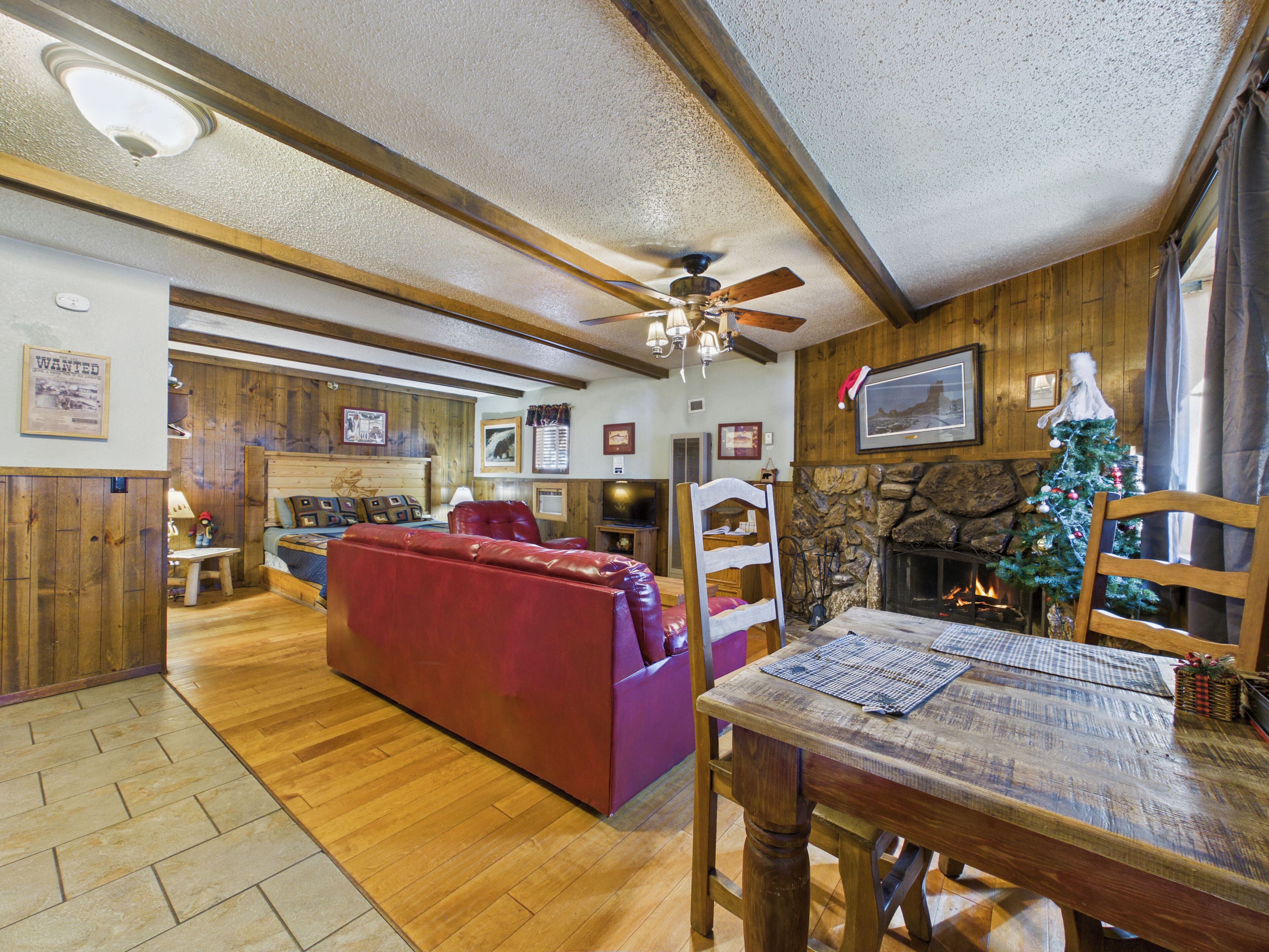A cozy living room with a fireplace, wooden walls, a red sofa, and a dining table.