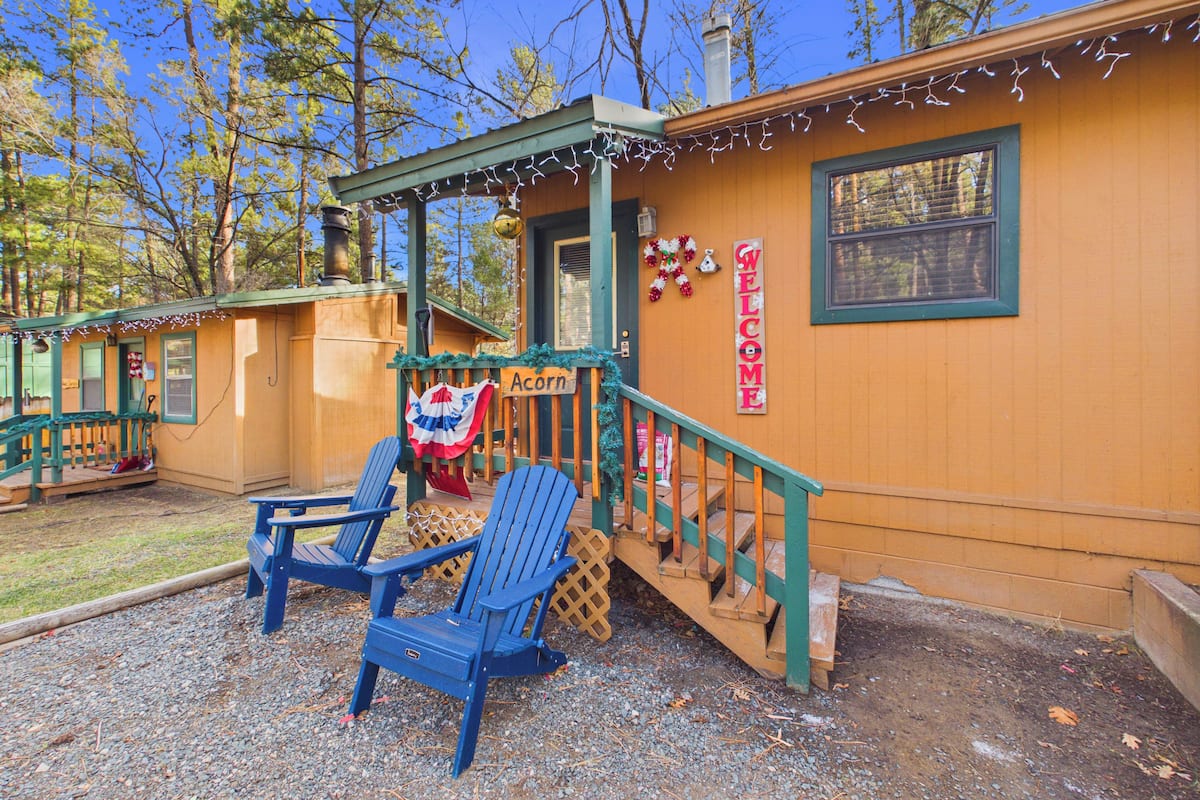Une cabane avec une véranda, des chaises Adirondack bleues, une pancarte de bienvenue et une guirlande décorative avec le mot « Bienvenue ».