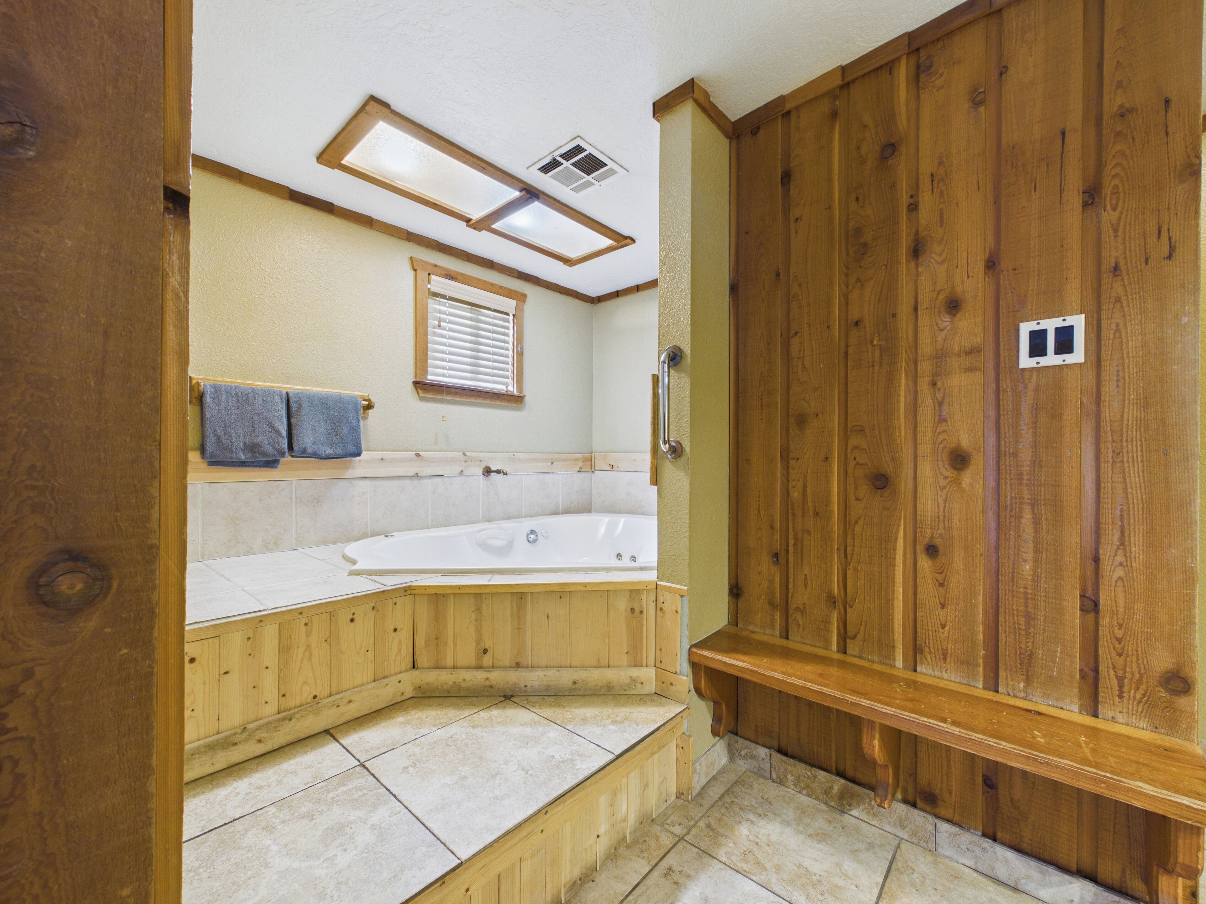 A bathroom with a wooden vanity, a bathtub, a window with blinds, and a towel rack.