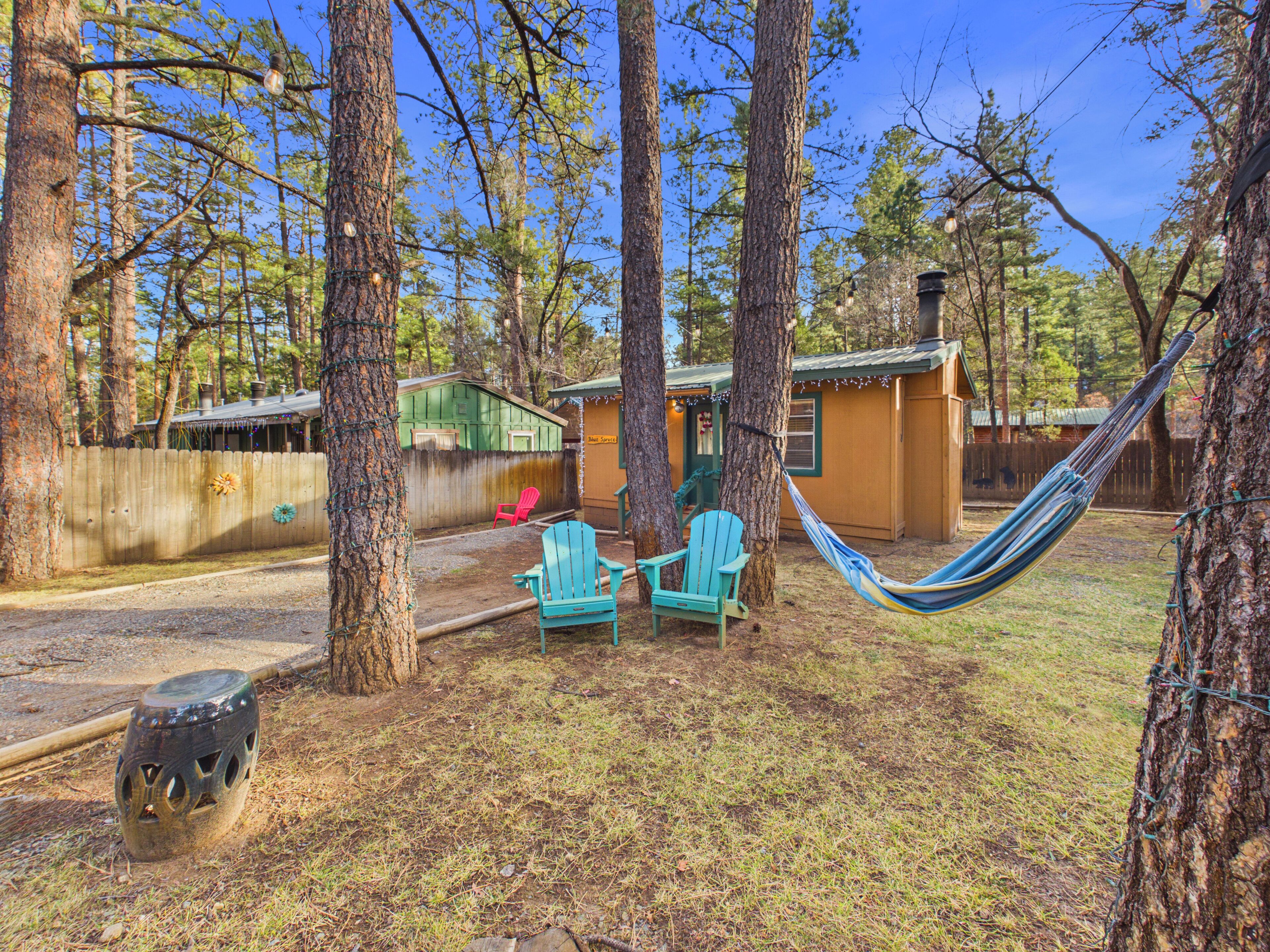 A fenced backyard with two blue Adirondack chairs, a hammock, and a small shed.