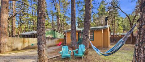 A fenced backyard with two blue Adirondack chairs, a hammock, and a small shed.