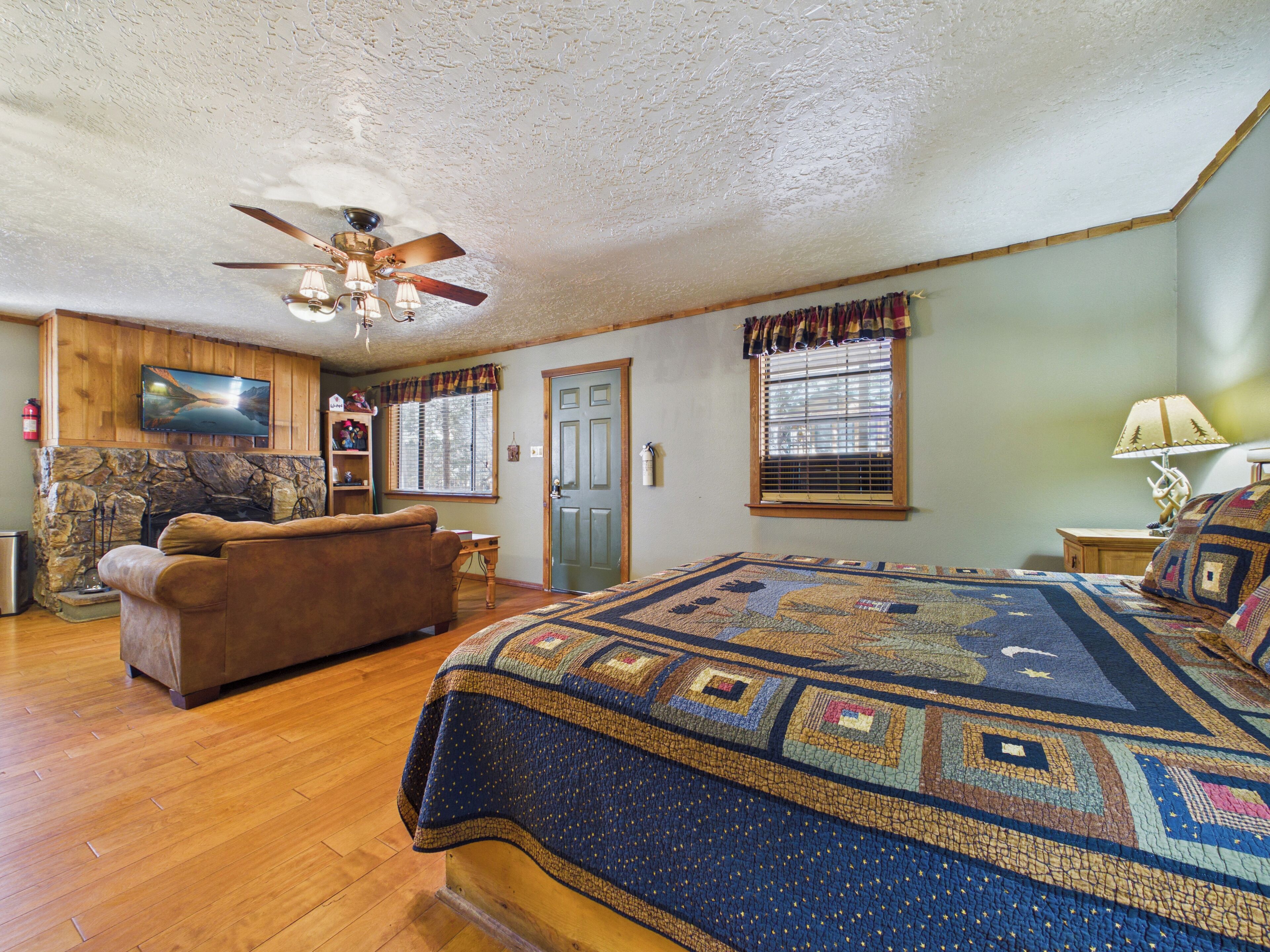 A cozy room with a bed, a sofa, a fireplace, a ceiling fan, and a television.