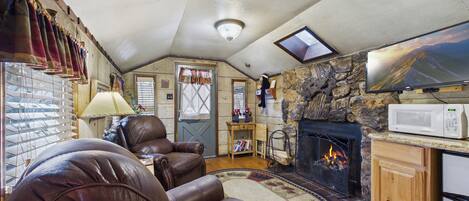 A cozy living room with leather chairs, a fireplace, a stone wall, a television, and a wooden cabinet.
