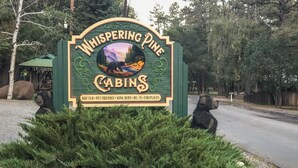 A sign for Whispering Pine Cabins with amenities like a hot tub, pet-friendly options, king beds, Wi-Fi, and fireplaces. - Whispering Pine Cabins (Ruidoso)