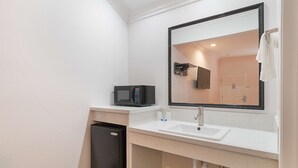 Een kleine badkamer met een witte wastafel, een zwarte magnetron en een kleine, zwarte koelkast.