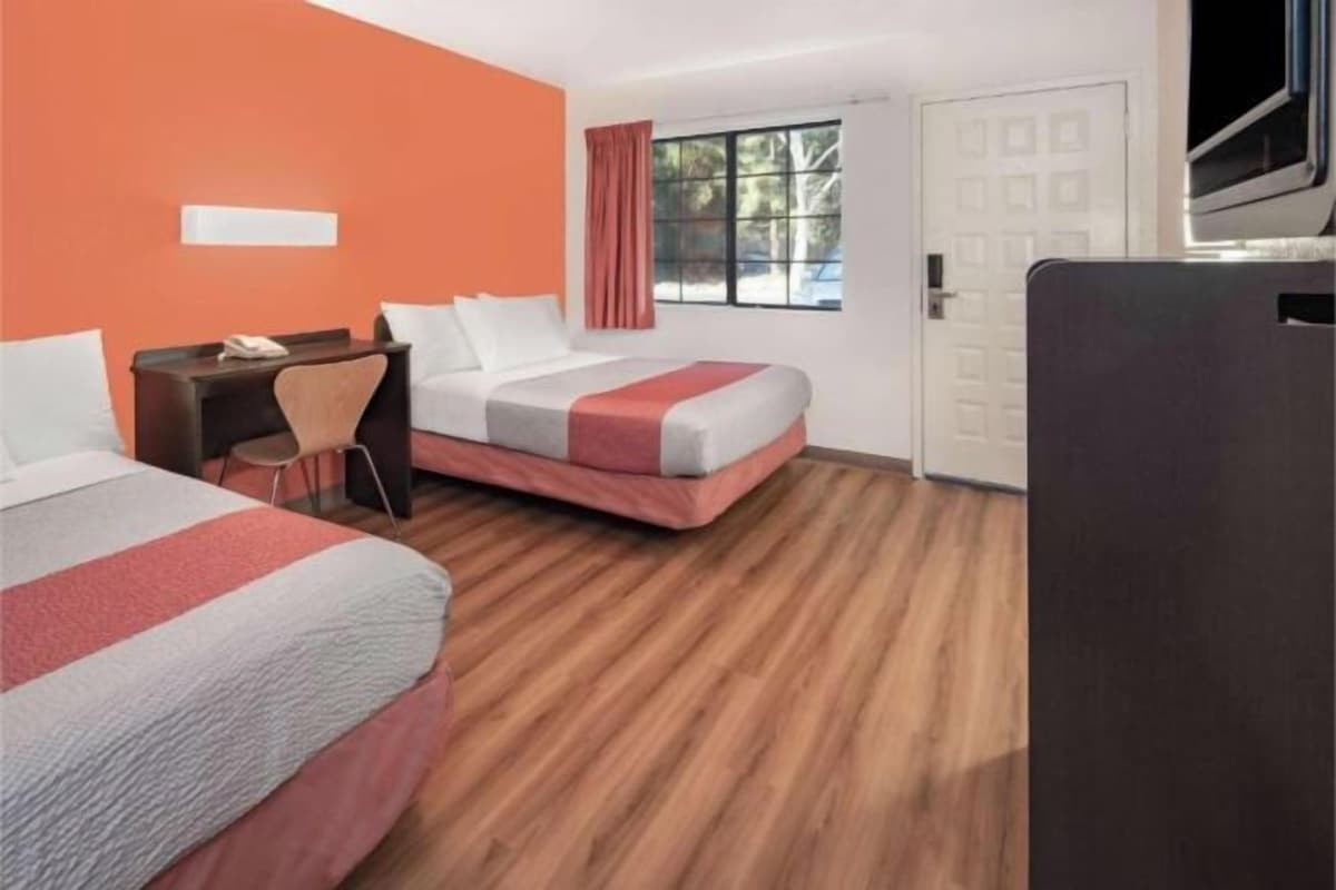 Habitación de hotel con dos camas, un escritorio, una silla y una ventana con cortinas.