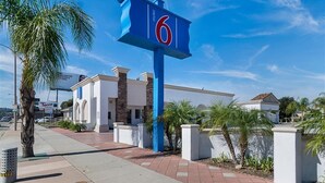 Een motel met een opvallend bord met het cijfer '6', een modern gebouw met plat dak en een palmboom op de voorgrond.