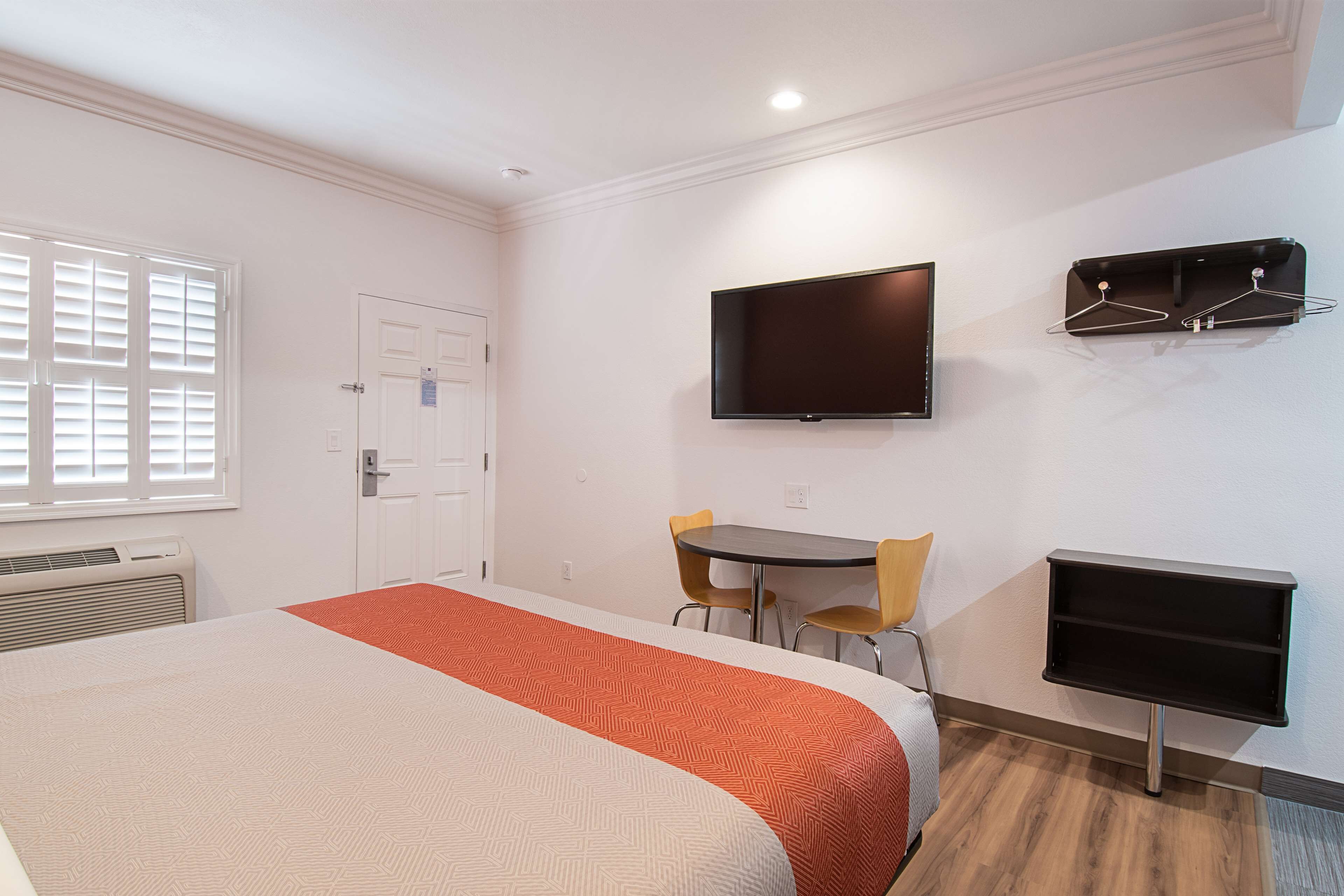 A hotel room with a bed, a TV, a desk with chairs, and a coat rack.