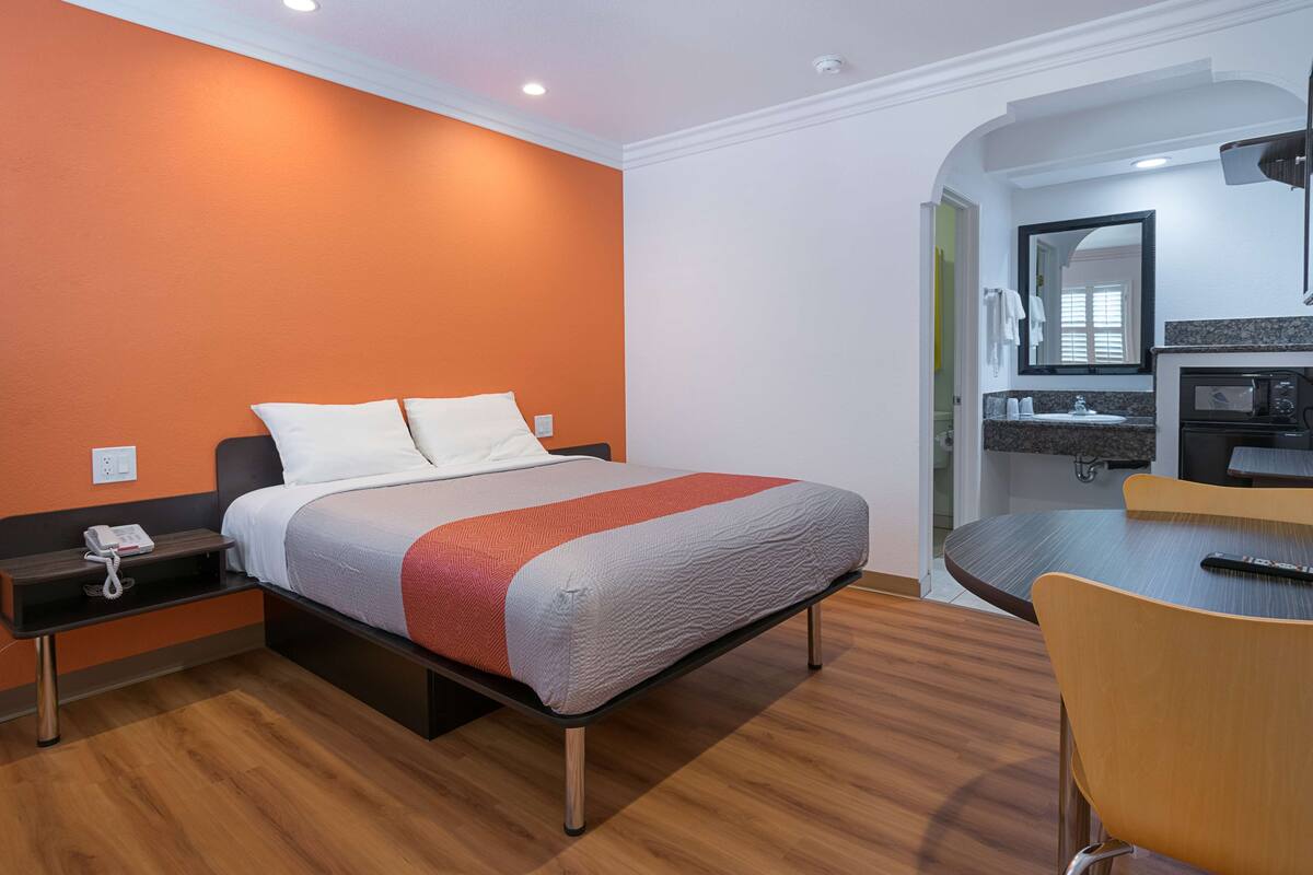 Une chambre d’hôtel comprenant un lit, une table de chevet avec un téléphone, une petite table avec des chaises, un four à micro-ondes et un lavabo dans la salle de bain attenante.