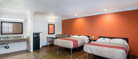 Habitación de hotel con dos camas, un escritorio, una silla, una kitchenette pequeña y un baño.