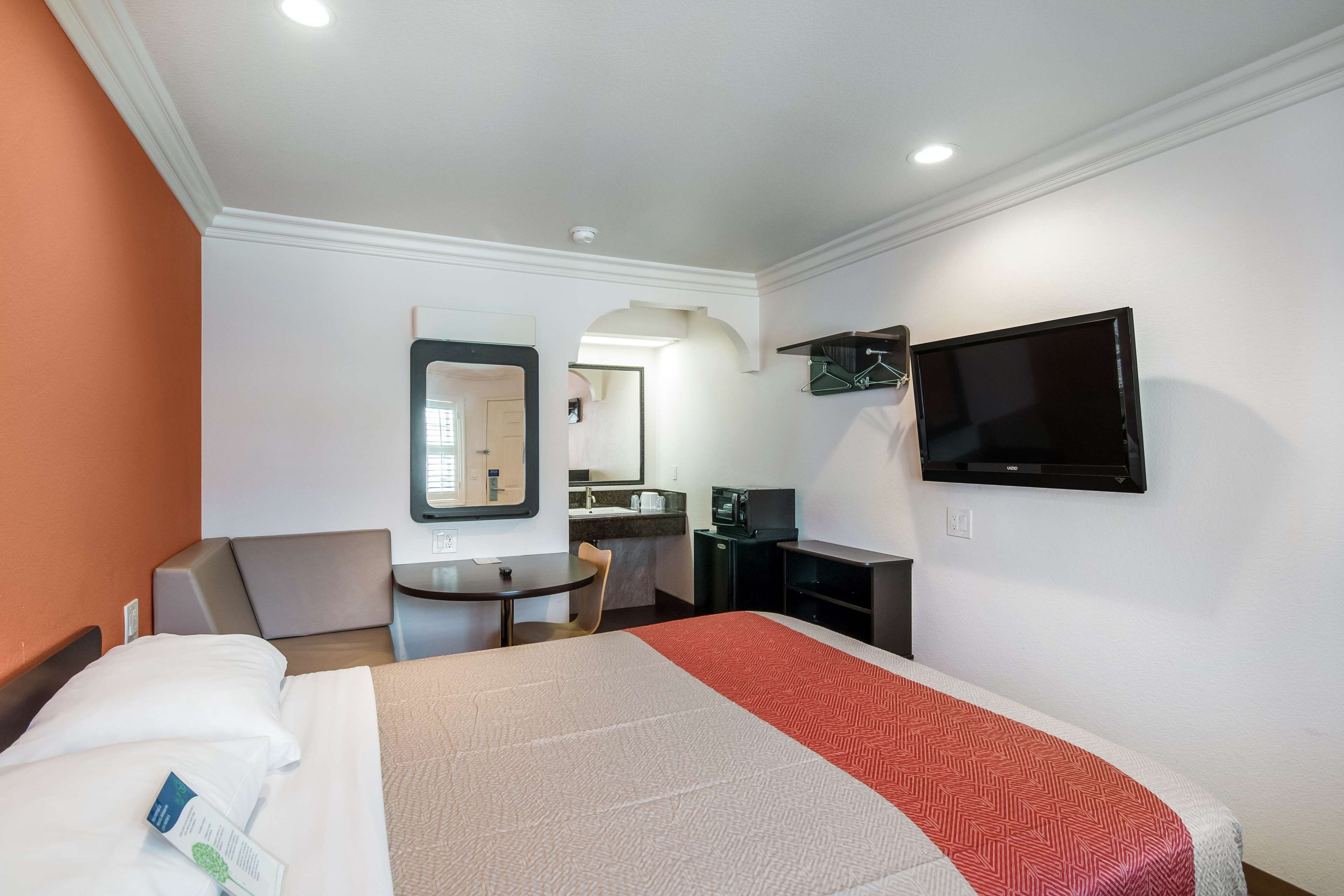 A hotel room with a bed, a desk, a chair, a television, and a mirror.