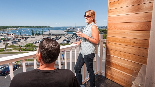 A balcony with a view of a marina and boats, a wooden wall, and a person standing on the balcony. - Rockland Harbor Hotel (Rockland)