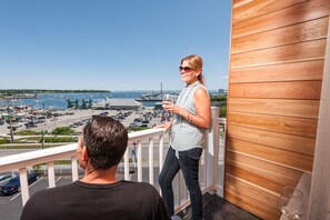 A balcony with a view of a marina and boats, a wooden wall, and a person standing on the balcony. - Rockland Harbor Hotel (Rockland)