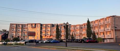 A multi-story hotel with balconies, a parking lot, and a street view.