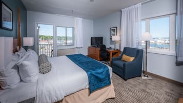 A hotel room with a bed, desk, chair, and large windows offering a view of the city.