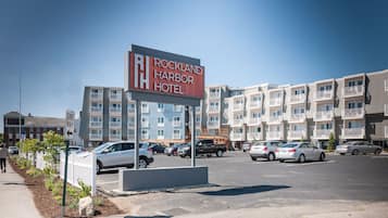 Señal de Rockland Harbor Hotel, con un estacionamiento y edificios de varios pisos al fondo.