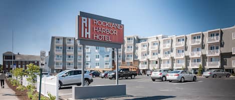 Señal de Rockland Harbor Hotel, con un estacionamiento y edificios de varios pisos al fondo.
