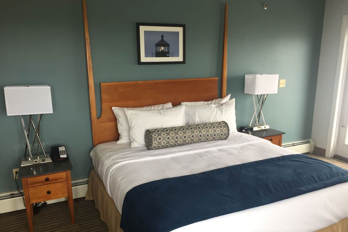 A hotel room with a large bed, two bedside tables, a nightstand, a framed picture on the wall, and a window.